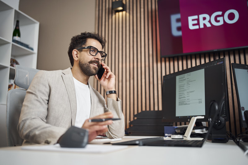 ERGO Mitarbeiter am Telefon vor ERGO Logo auf dem Bildschirm