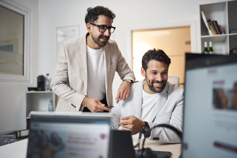 Zwei ERGO Kollegen lachen gemeinsam vor dem Monitor